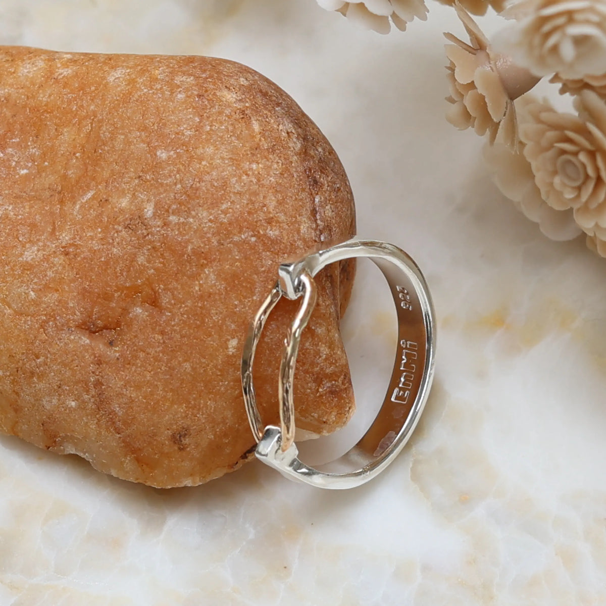Silver ring on a textured stone surface with floral elements