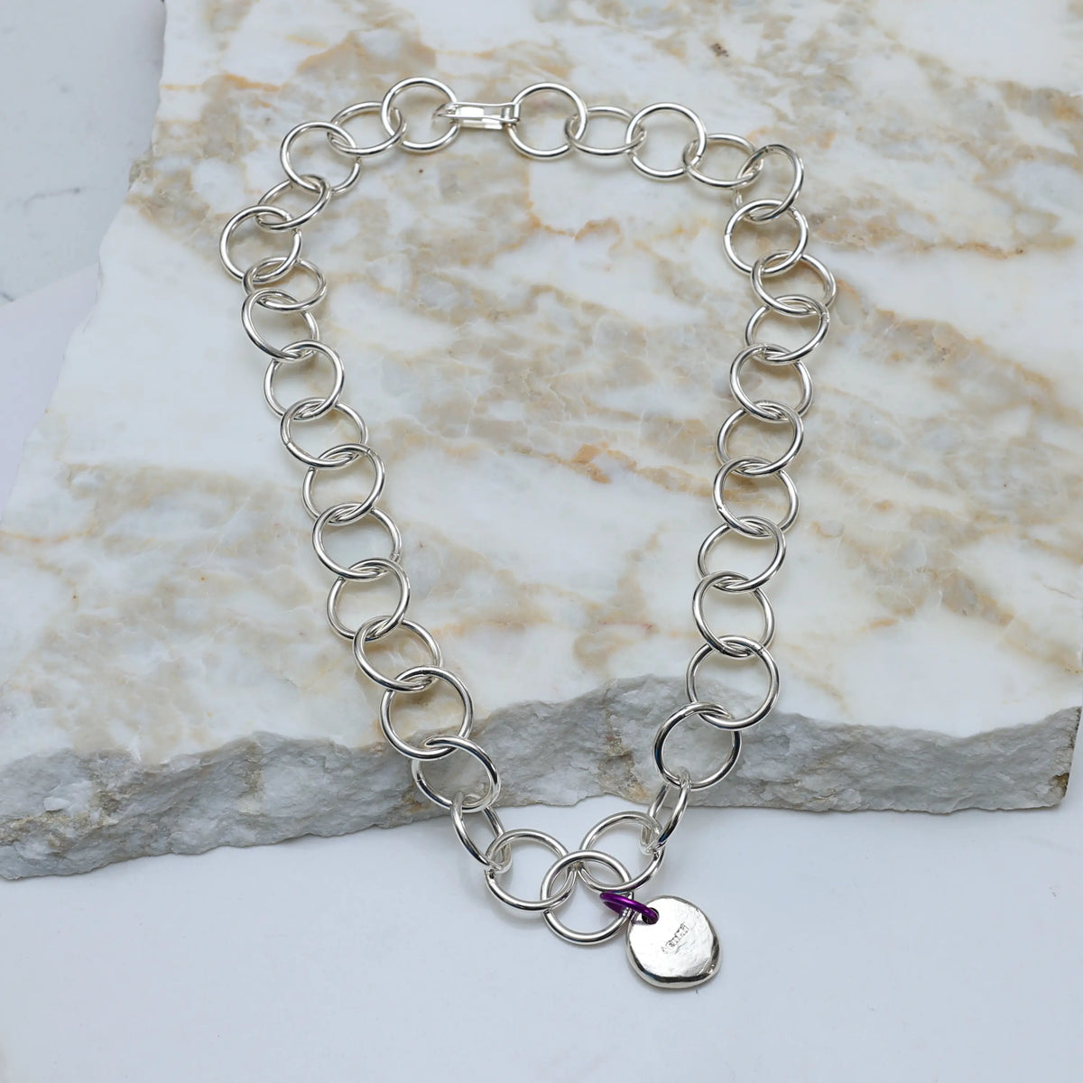 Silver chain bracelet with a heart-shaped tag on a marble surface