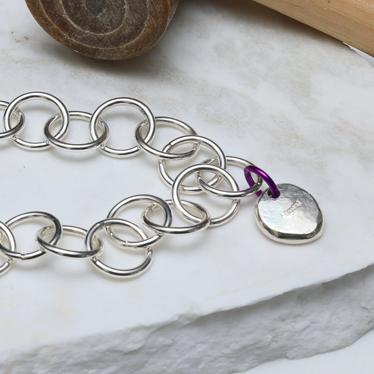 Silver chain bracelet with a heart-shaped tag on a marble surface