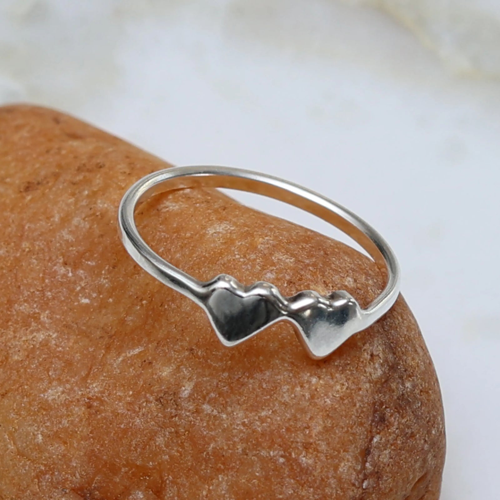Silver ring with double heart design on a stone surface