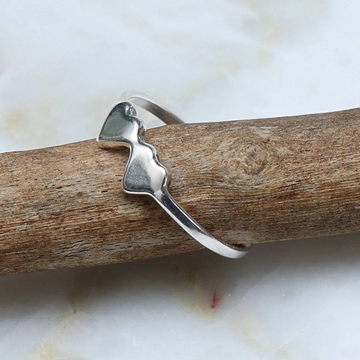 Silver ring on a piece of driftwood with a white marble background