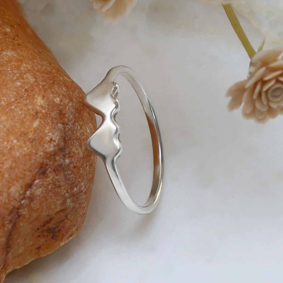 Silver double heart ring on a textured surface with floral elements