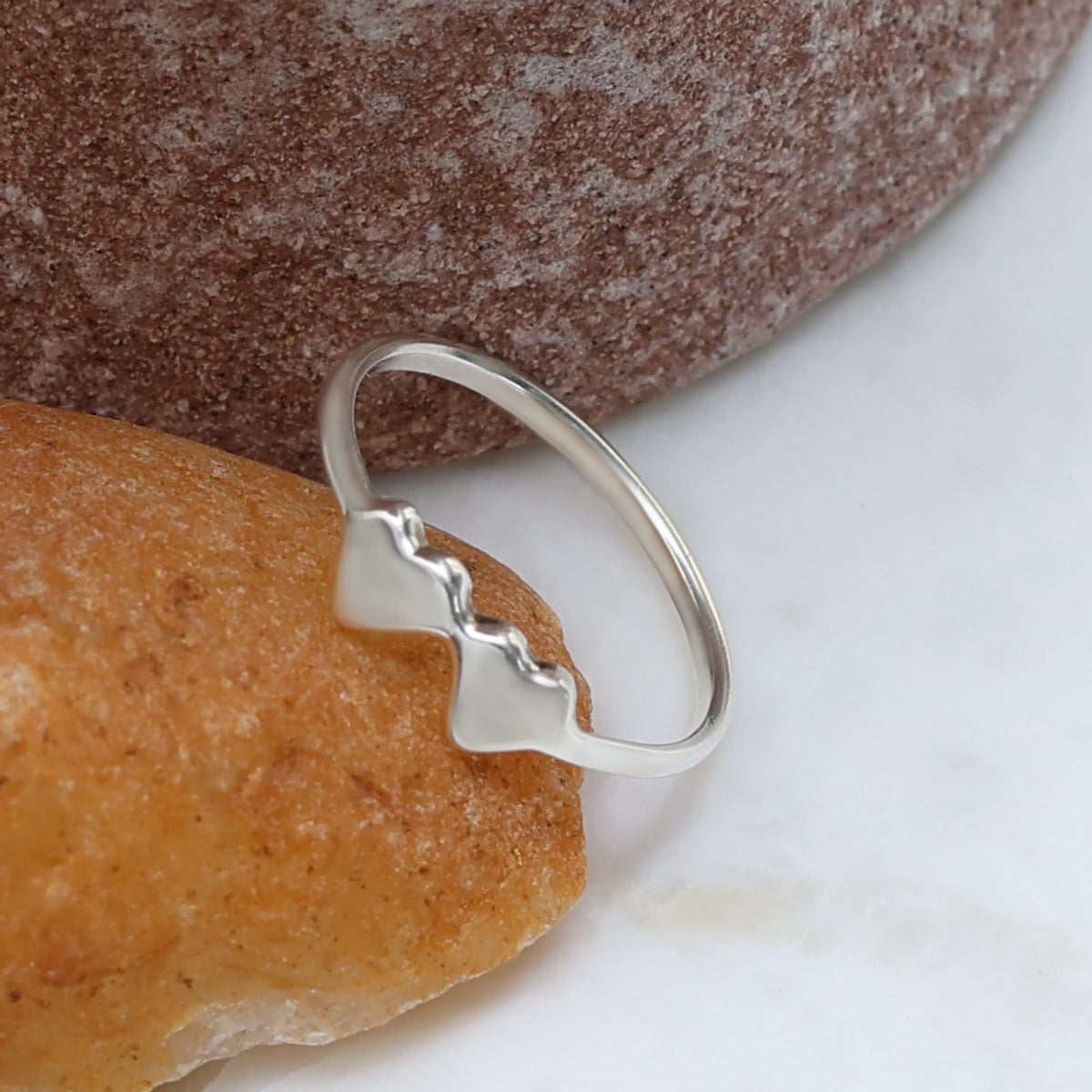 Silver ring with double heart design on a stone surface